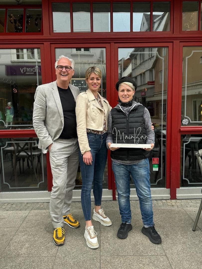 Die Mainbar-Inhaberin Ramona Krines (Mitte) veranstaltet am 27. April bei freiem Eintritt ein Weinfest für einen guten Zweck. Ein Teil des Erlöses geht an die Schweinfurter Kindertafel e.V. und sie wird bei der Umsetzung des Weinfestes unterstützt von den beiden Botschaftern der Kindertafel Steffi List (rechts) und Peter Kruse (links). Foto: Frieda Siegel