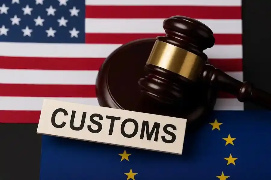 Gavel mit „Customs“-Schild zwischen USA- und EU-Flagge, Symbol für Zollabkommen und Handelskonflikte.