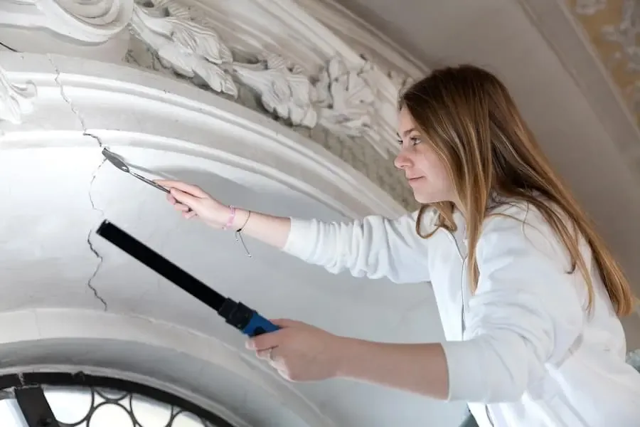 Junge Frau bei der Ausbildung im Handwerk bearbeitet mit Werkzeug eine historische Stuckdecke