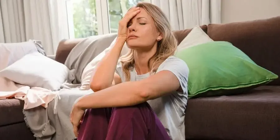 Frau sitzt erschöpft auf dem Boden, stützt Kopf mit der Hand – Symbolbild für Beschwerden bei Endometriose oder Wechseljahren
