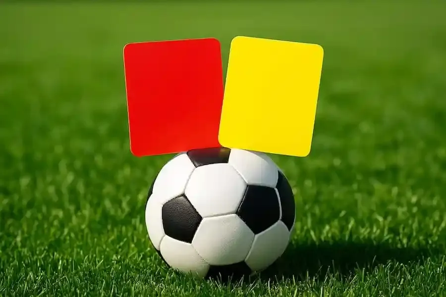 Rote und gelbe Karte als Symbolfoto auf einem Fußball auf grünem Rasen
