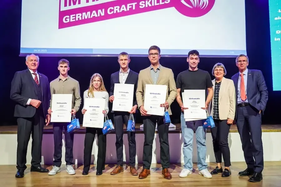 Gruppenfoto während der Auszeichnungsfeier zur Deutschen Meisterschaft im Handwerk 2025: junge Nachwuchskräfte stehen mit Urkunden auf einer Bühne, umgeben von Vertreterinnen und Vertretern des bayerischen Handwerks.