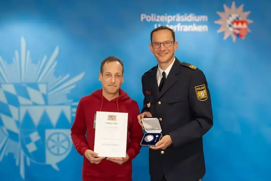 Übergabe einer Auszeichnung im Polizeipräsidium Unterfranken: Eine geehrte Person mit Urkunde neben uniformiertem Polizeivertreter