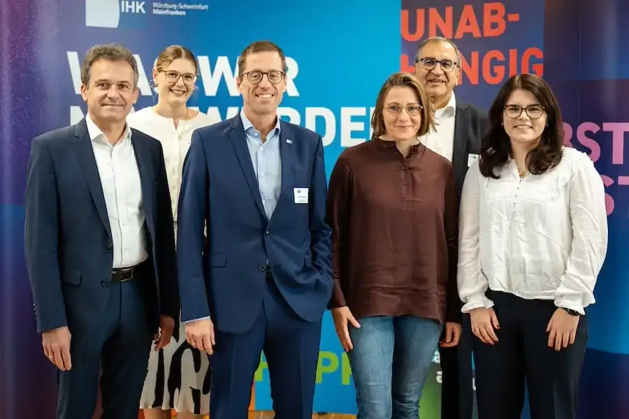 Gruppenfoto mehrerer Teilnehmerinnen und Teilnehmer beim Mainfränkischen Ausbildertag in der IHK Schweinfurt vor farbigem Hintergrund.