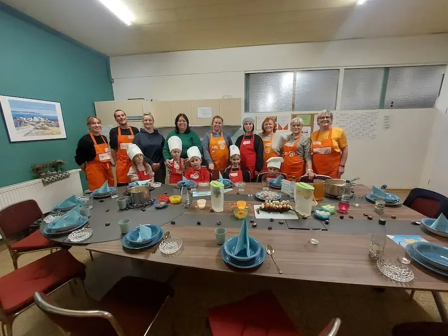 Gruppe aus Kindern und Helferinnen und Helfern der Tafel Schweinfurt steht in einer Küche vor einem gedeckten Tisch beim Ernährungsprojekt.