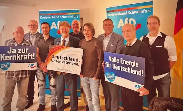 Gruppenaufnahme einer AfD-Veranstaltung des Kreisverbands Schweinfurt-Land mit politischen Bannern und Plakaten im Hintergrund.