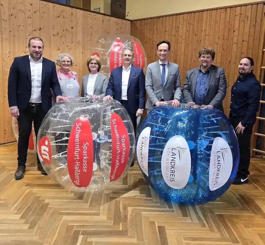 Gruppenfoto bei der Übergabe neuer Bubble Balls im Karl-Beck-Haus Reichmannshausen mit großen transparenten Spielbällen in der Turnhalle.