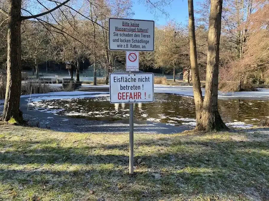Warnschild vor Eisbruchgefahr an zugefrorenem Weiher bei Minusgraden