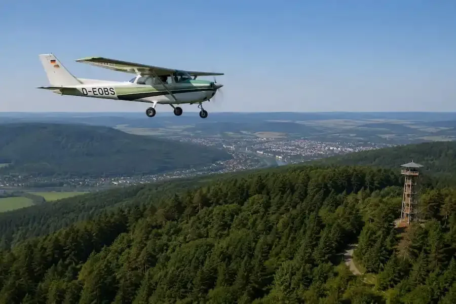 Kleinflugzeug zur Luftbeobachtung fliegt über Wälder und Hügellandschaft in Unterfranken bei hoher Waldbrandgefahr