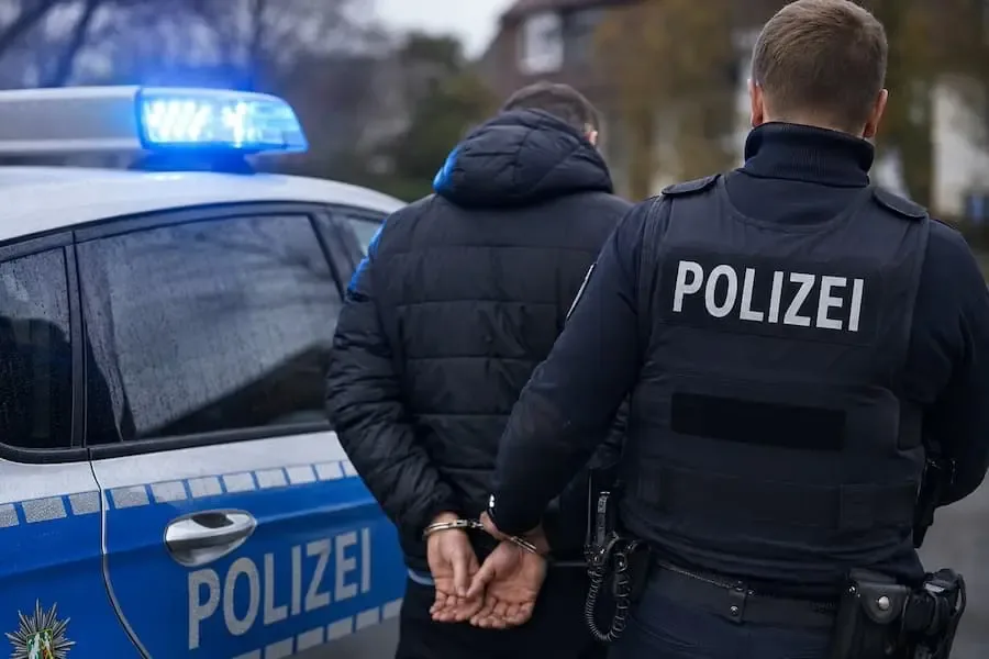 Polizeibeamter führt einen festgenommenen Tatverdächtigen nach einem räuberischen Diebstahl in Schweinfurt zu einem Streifenwagen.
