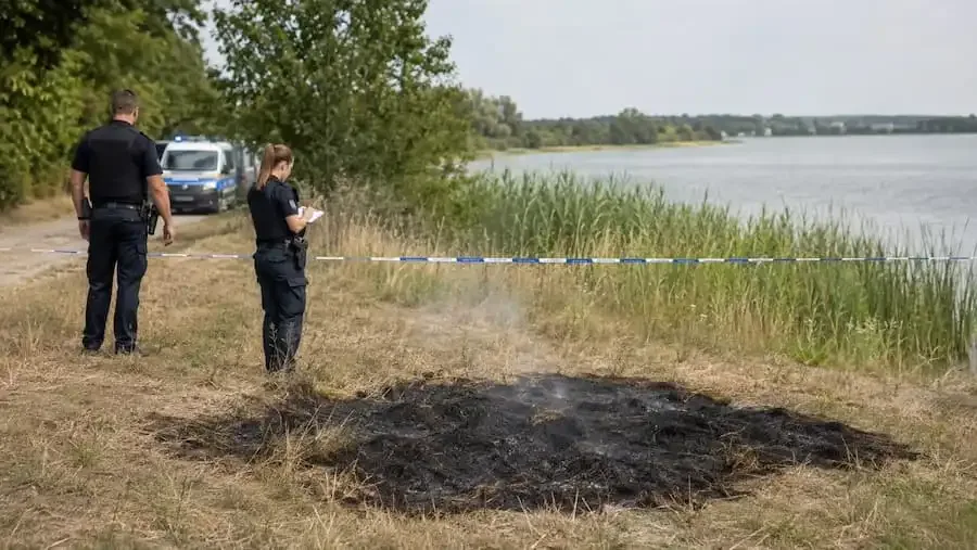 Polizeibeamte untersuchen eine verbrannte Wiesenfläche an einem See