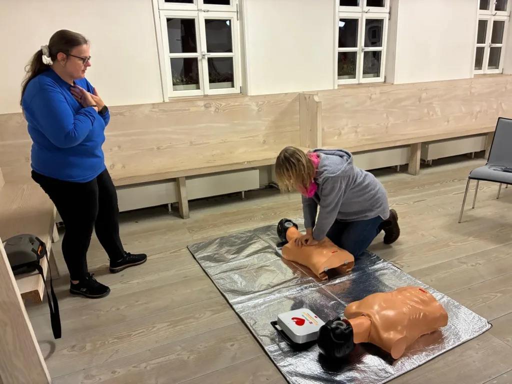 Teilnehmerin übt bei einer Erste-Hilfe-Veranstaltung in Gochsheim die Herzdruckmassage an einer Reanimationspuppe. Daneben liegt ein Defibrillator.