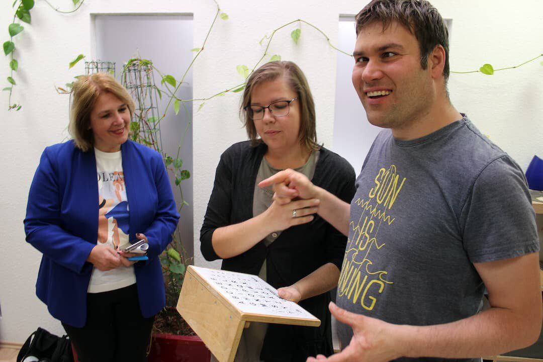 (Foto: Reto Glemser): Hilfsmittel aus der gestützten Kommunikation stärken die Fähigkeit, sich auszudrücken: Tobias Schimmel begrüßt damit die CSU-Landtagsabgeordnete Martina Gießübel (links), die von Gruppenleiterin Sandra Thein durch die Schweinfurter Tagesförderstätte für Menschen mit Autismus geführt wird. (Foto: Reto Glemser)
