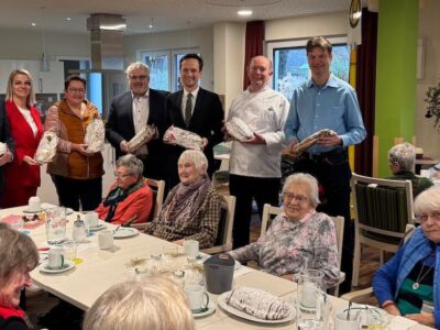 Christstollenspende in der AWO Tagespflege am Sonnenteller in Dittelbrunn mit (hintere Reihe, von links) Stefan Rottmann (stellv. Vors. AWO Bezirksverband), AWO-Pflegedienstleiterin Lejla Gallagher, Jugendhilfezentrumsleiterin Stefanie Kimmel, Bürgermeister Willi Warmuth, Landrat Florian Töpper, Innungsobermeister Gerhard Götz und Bäckermeister Udo Dietmann. Foto: Andreas Lösch/Landratsamt Schweinfurt