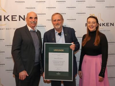 Der Präsident des Fränkischen Weinbauverbands Artur Steinmann (links) übergibt zusammen mit der 66. Fränkischen Weinkönigin Lisa Lehritter (rechts) an Artur Baumann (in der Mitte) den Goldenen Bocksbeutel, die höchste Auszeichnung der fränkischen Weinwirtschaft. Foto: Rudi Merkl / Fränkischer Weinbauverband
