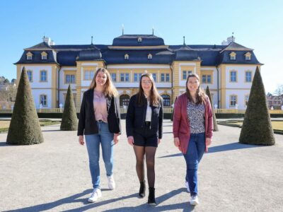 Königlicher Hintergrund für die beiden Aspirantinnen für das Amt der 67. Fränkischen Weinkönigin: Antonia Kraiß aus Nordheim am Main (links) und Vanessa Nüßlein aus Theilheim (rechts) und die amtierende 66. Fränkische Weinkönigin Lisa Lehritter in der Mitte vor dem Schloss Veitshöchheim, der ehemaligen Sommerresidenz der Fürstbischöfe von Würzburg und später der Könige von Bayern. Foto: Rudi Merkl / Gebietsweinwerbung Frankenwein-Frankenland GmbH